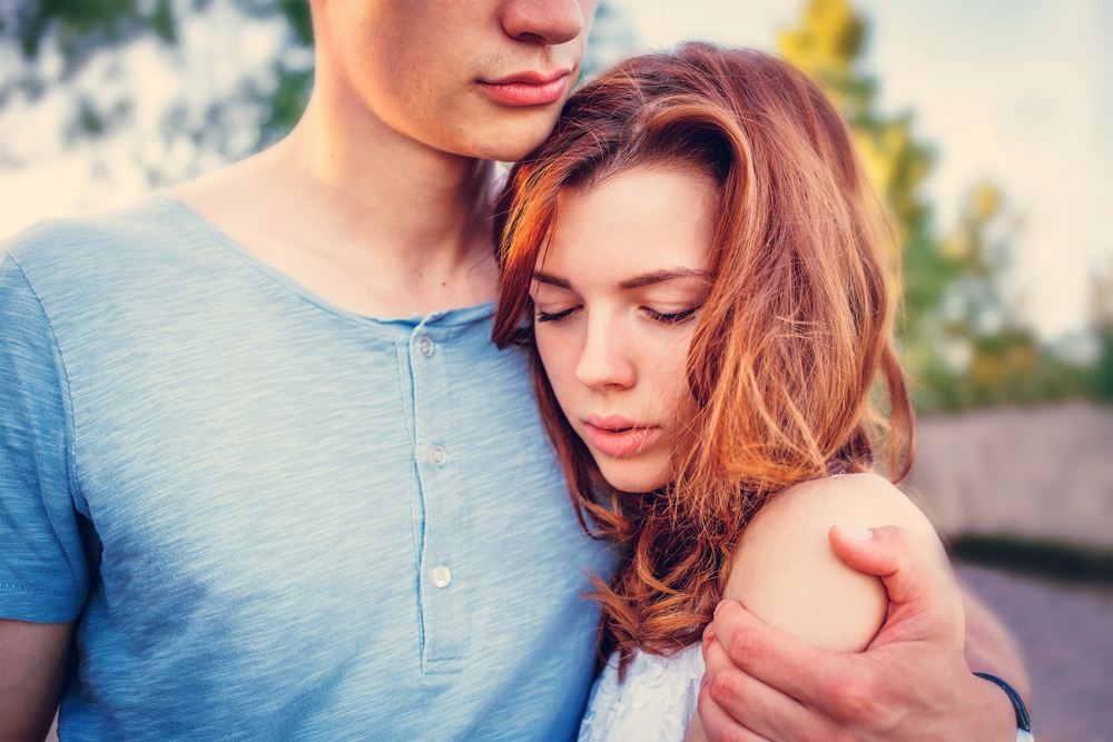 恋人に抱きつきながらうつむく女性